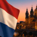 A widescreen 5:3 composite image showing the Dutch flag in the foreground, Amsterdam city skyline with modern office towers and canals at sunset, and translucent Forex candlestick charts overlaid in the sky to represent the Netherlands’ dynamic trading market.