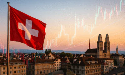 A widescreen composite with a 5:3 aspect ratio featuring the Swiss flag waving in the foreground, Zurich’s skyline at dusk with landmarks like Grossmünster, overlaid by translucent Forex candlestick charts and line graphs, symbolizing Switzerland’s dynamic trading landscape.