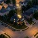Aerial view of an American suburban neighborhood at dusk with a subtle Bitcoin-shaped golden light among the homes, representing growing household cryptocurrency adoption.